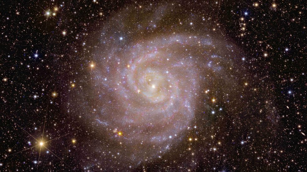 Immagine che raffigura una galassia a spirale vista di fronte, immersa in un fitto campo di stelle