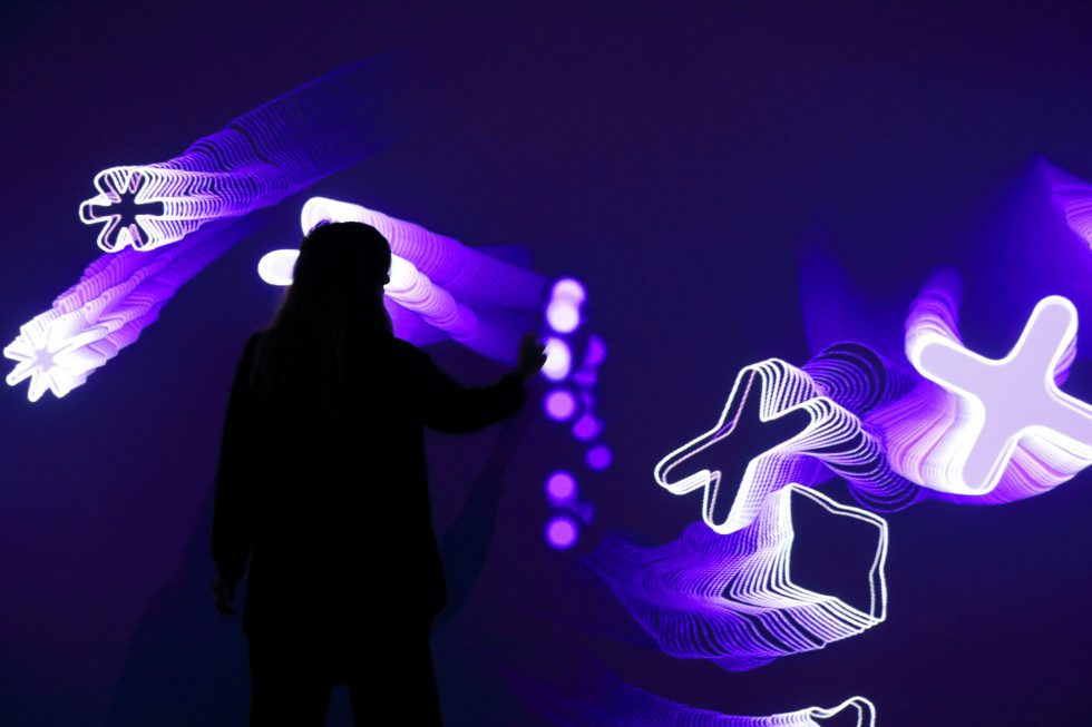 immagine che raffigura una persona in silhouette vista di spalle osserva un'installazione artistica luminosa in un ambiente scuro