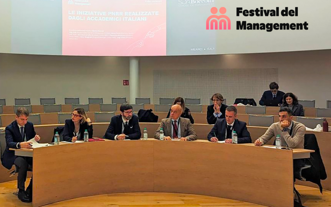 Immagine che raffigura un panel di sei relatori, cinque uomini e una donna, seduti a un lungo tavolo curvo in legno chiaro all'interno di un auditorio per il Festival del Management