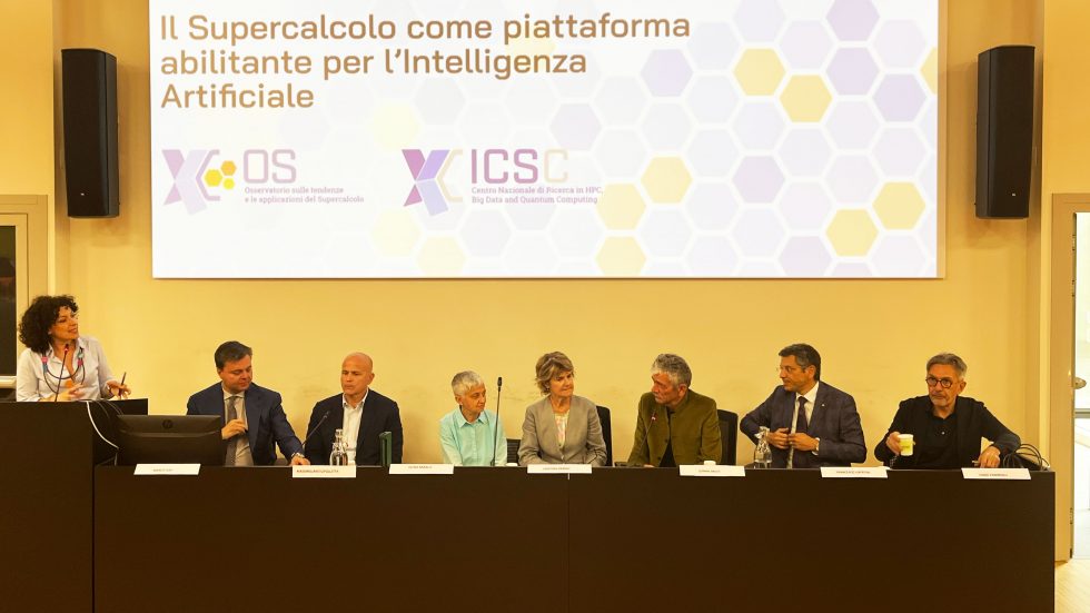 Immagine che raffigura un tavolo di relatori durante un convegno, con una moderatrice al podio sulla sinistra e sette ospiti seduti incontro Supercalcolo